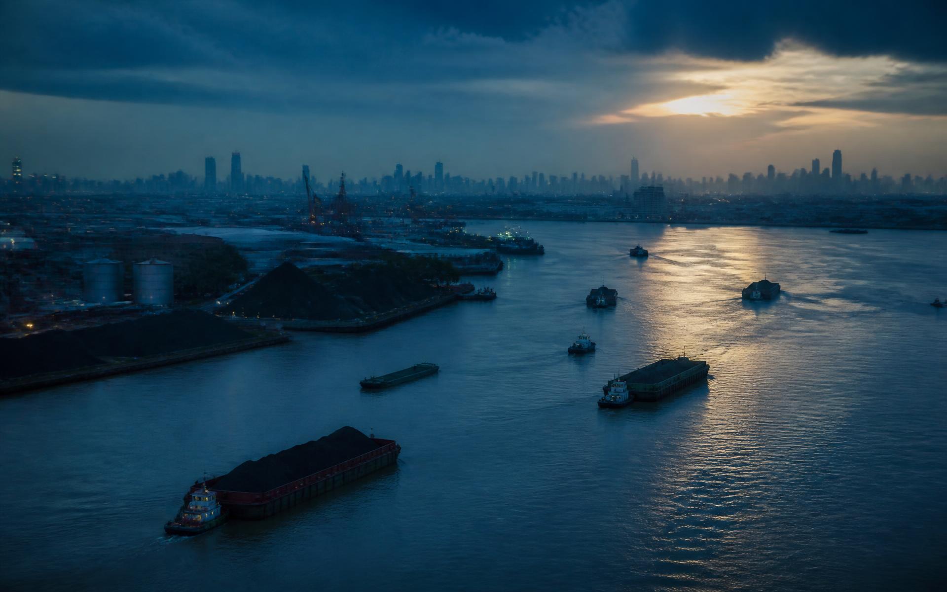 Barges on an Indonesian waterway at dusk with the Jakarta skyline beyond